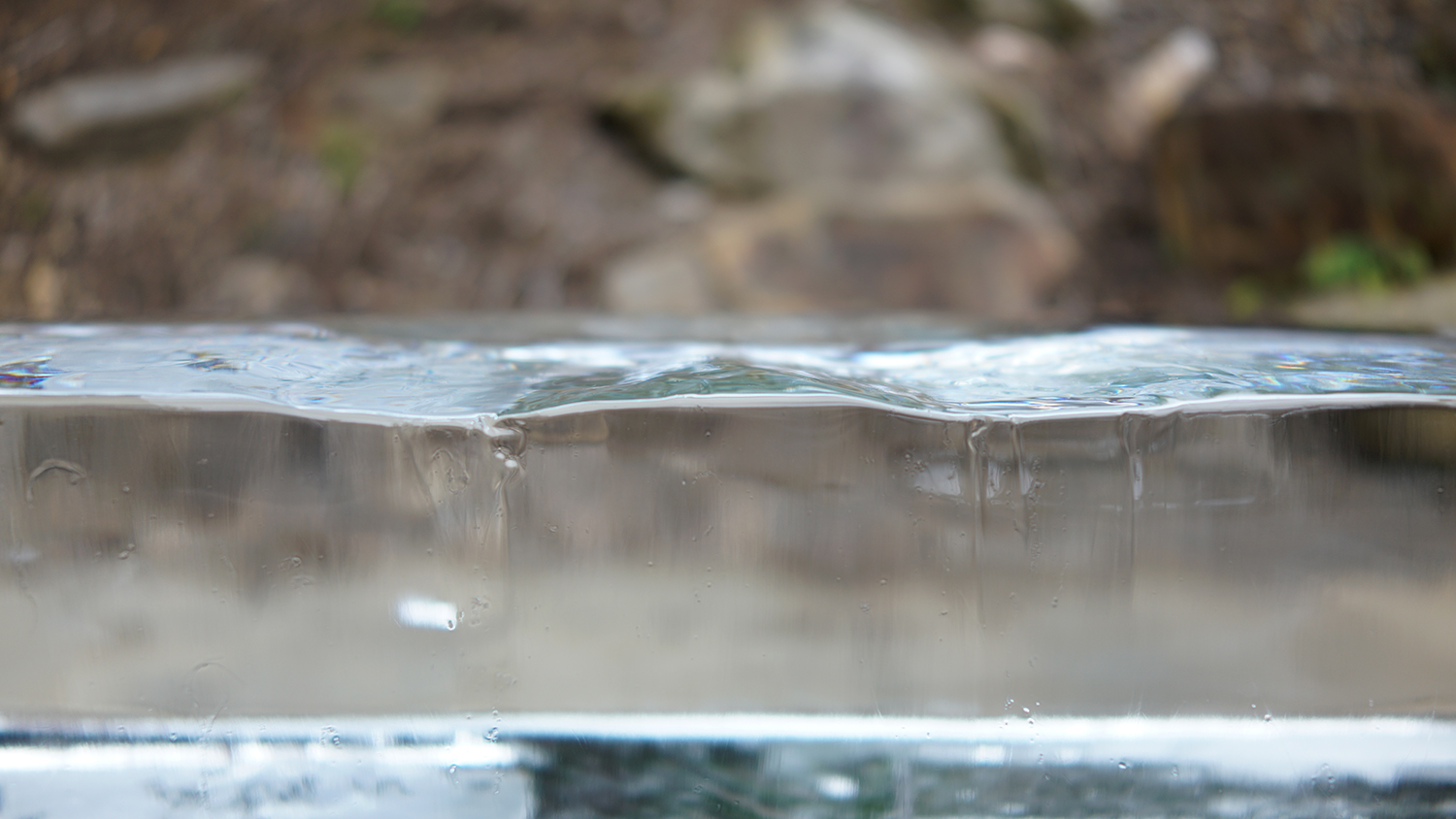 All That Is Solid Melts Into Air, 2025, color digital print, 24 x 13.5<br><br>Describing how the bourgeoisie preserve control Karl Marx wrote “all that is solid melts into air.” New becomes old before it can solidify. People constantly experience changing realities and truths. Uncertainty cloaks the facts. Dressed in a suit and tie, similar to John Cage in his 1959 “Water Walk,” I sit on a bench of ice. ReViewing Black Mountain College Conference attendees partake too. Accompanying the performance, a speaker broadcasts the sound of melting ice. In “Water Walk,” Cage created music from sounds of overlooked everyday water related items, while “All That Is Solid Melts Into Air’s” soundscape makes audible the almost imperceptible melody of melting ice. Wet bottoms from the melting ice imprint and remind us of our experience of unrelenting change and ambiguity.