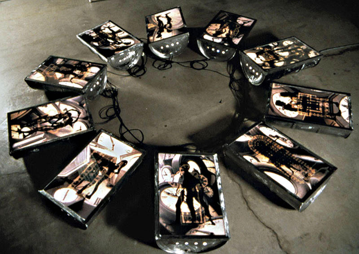 Chronos, 1999, installation view, color transparencies, 10 halved fifty-five gallon barrels (light box), 240 x 240<br><br>Ouranos covered and copulated with Gaia until their son Kronos became angered and castrated him, separating sky from earth and becoming known as the creator of time. The color transparencies overlay male and female figures with ten influential cathedrals and Arman clocks.