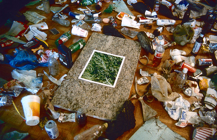 Your Litter Invades Your Space, 1998, installation detail, C-Print, 14 x 11, granite, 33 x 22, collected trash, 144 x 84<br><br>Viewers collect trash outside the gallery and place around a photograph of verdant grass on granite.